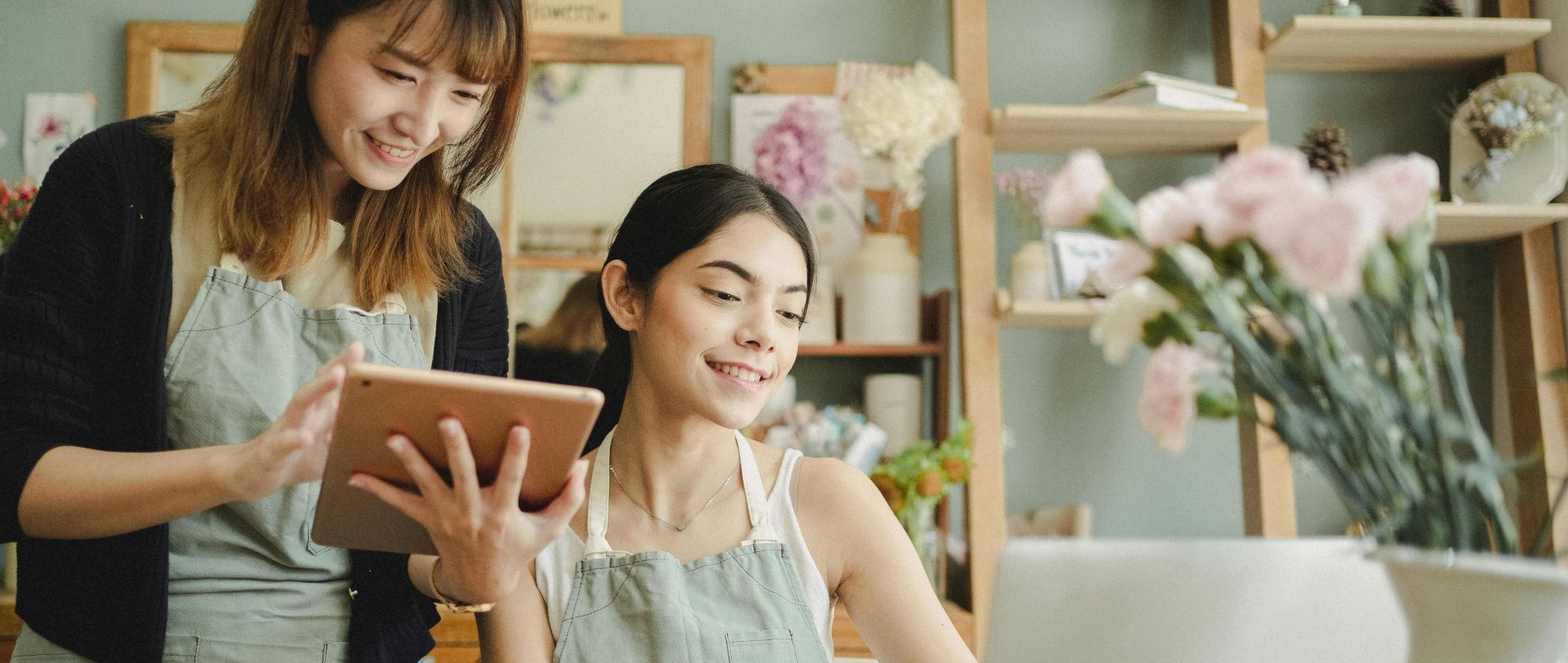 Two smiling florists working together with digital devices in a flower shop.