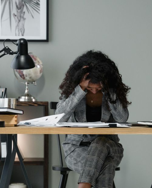 A frustrated businesswoman sitting at a desk, stressed in a modern office setting.