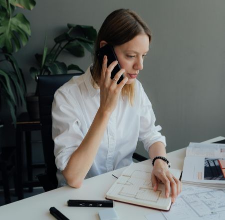 Focused woman architect discussing floor plans on the phone in an office setting.